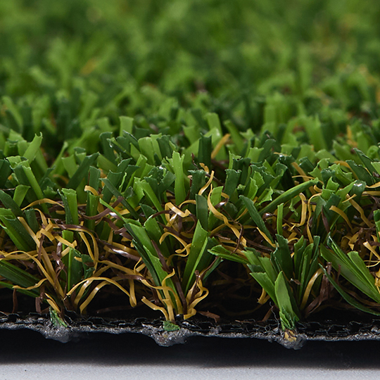 Close-up side view of green and tan turf fibers above a dark backing