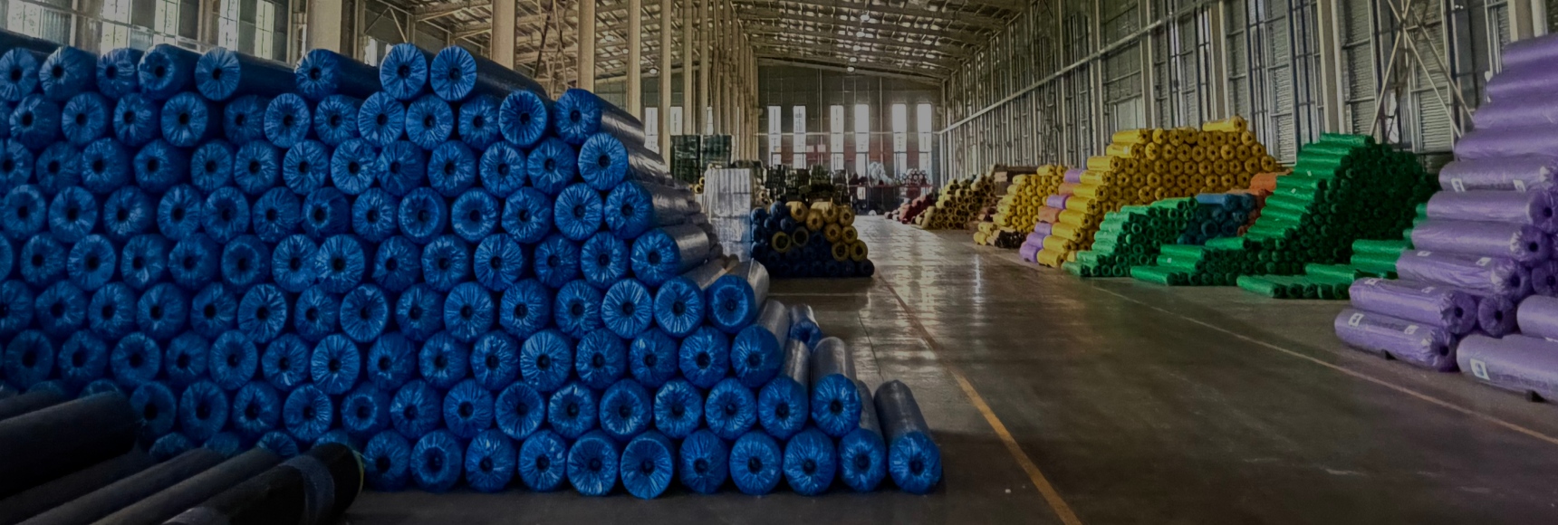 Indoor warehouse with rolls of rolled artificial turf in blue, yellow, green, and purple